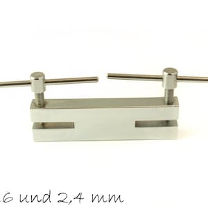 Peut inclure: Un outil de poinçonnage en métal argenté avec deux poignées réglables. L'outil comporte deux trous, l'un de 1,6 mm et l'autre de 2,4 mm de diamètre. Le texte "Ø 1,6 und 2,4 mm" est imprimé sous l'outil.