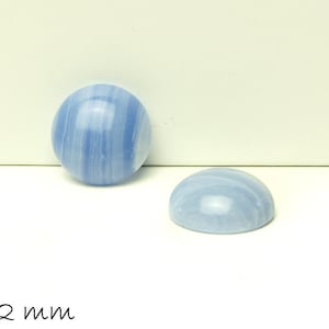 Könnte beinhalten: Zwei blaue Achat-Cabochons, jeweils 12 mm im Durchmesser, mit einem wirbelnden, marmorierten Muster. Die Cabochons werden auf einer weißen Oberfläche gezeigt.