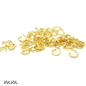 Op de afbeelding: Een stapel gouden springringen, elk met een diameter van 5 mm. De ringen zijn verspreid over een witte achtergrond.
