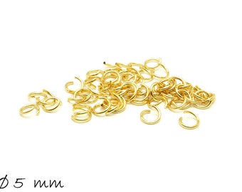 May include: A pile of gold jump rings, each measuring 5 mm in diameter. The rings are scattered on a white background.