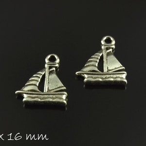 Pode incluir: Dois pingentes de barco a vela prateados, cada um medindo 20 mm por 16 mm. Os pingentes são detalhados com uma vela e um casco.