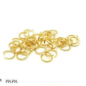 Könnte beinhalten: Ein Haufen goldener Sprungringe, jeder mit einem Durchmesser von 7 mm. Die Ringe sind in einem zufälligen Muster angeordnet, wobei sich einige überlappen.