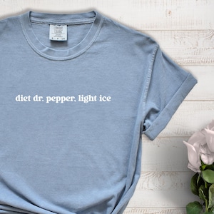 May include: A light blue t-shirt with the text "diet dr. pepper, light ice" in white. The shirt has a crew neck and short sleeves. The shirt is made of a soft material.