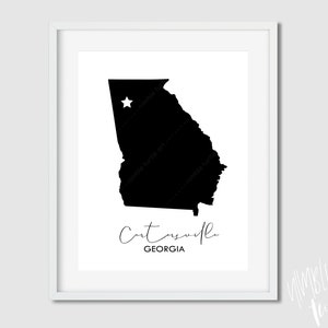 May include: A framed black and white print featuring the silhouette of the state of Georgia. A star marks a location within the state. The word "Catonsville" is written in cursive below the map, with "Georgia" below it.