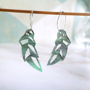 May include: A pair of green acrylic earrings shaped like a stylised leaf with a silver hoop.