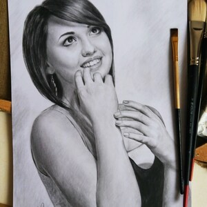 Puede incluir: Un dibujo a l&aacute;piz en blanco y negro de una mujer con el pelo corto y casta&ntilde;o, sonriendo y mirando hacia arriba. La mujer lleva una camiseta sin mangas y tiene las manos cerca de la cara.