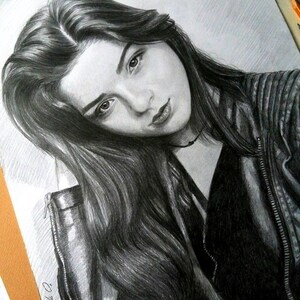 Puede incluir: Dibujo a l&aacute;piz en blanco y negro de una mujer con el pelo largo y oscuro que lleva una chaqueta de cuero negra. El dibujo est&aacute; sobre un fondo blanco.