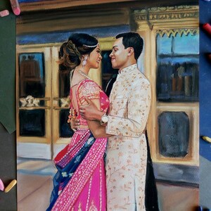 K&ouml;nnte beinhalten: Eine Pastellzeichnung eines Paares in traditioneller indischer Hochzeitskleidung. Die Frau tr&auml;gt ein rosafarbenes und blaues Sari mit goldenen Stickereien. Der Mann tr&auml;gt eine wei&szlig;e Sherwani mit goldenen Stickereien. Sie stehen eng beieinander und l&auml;cheln sich an. Die Zeichnung ist vor dem Hintergrund eines Geb&auml;udes mit kunstvollen Details.