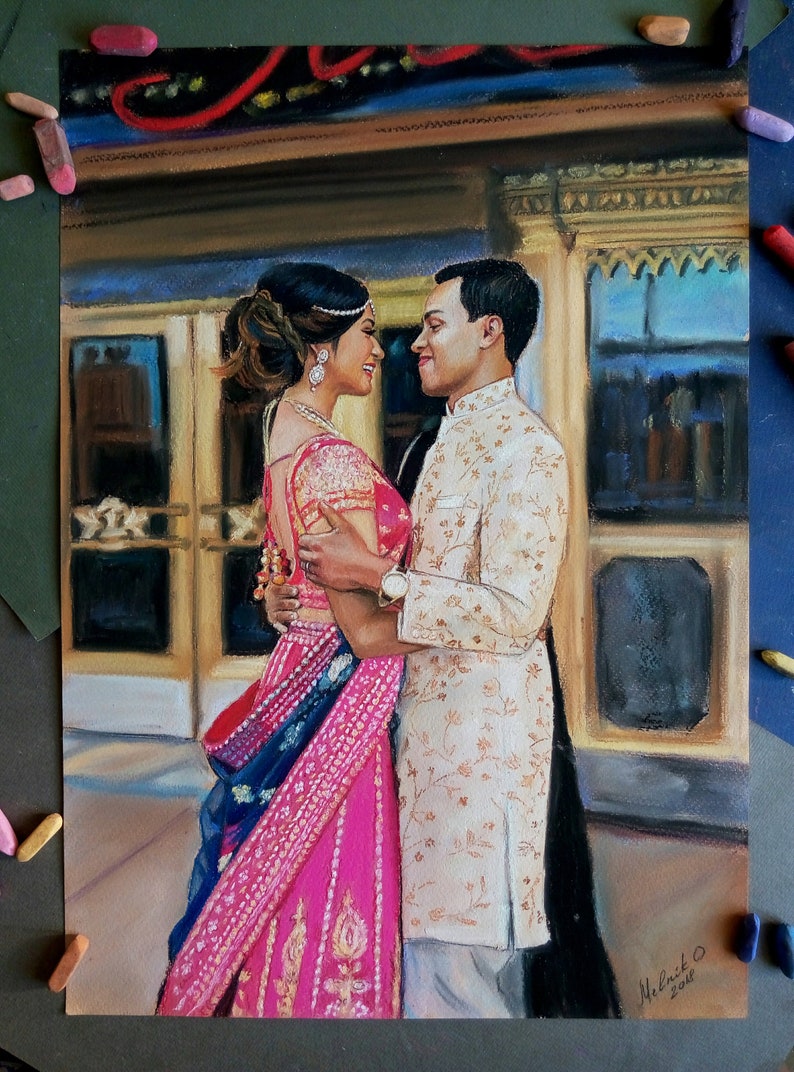 K&ouml;nnte beinhalten: Eine Pastellzeichnung eines Paares in traditioneller indischer Hochzeitskleidung. Die Frau tr&auml;gt ein rosafarbenes und blaues Sari mit goldenen Stickereien. Der Mann tr&auml;gt eine wei&szlig;e Sherwani mit goldenen Stickereien. Sie stehen eng beieinander und l&auml;cheln sich an. Die Zeichnung ist vor dem Hintergrund eines Geb&auml;udes mit kunstvollen Details.