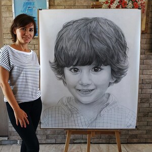May include: A black and white pencil drawing of a young boy with short brown hair, wearing a plaid shirt. The drawing is on a large piece of paper and is being held up by a woman.