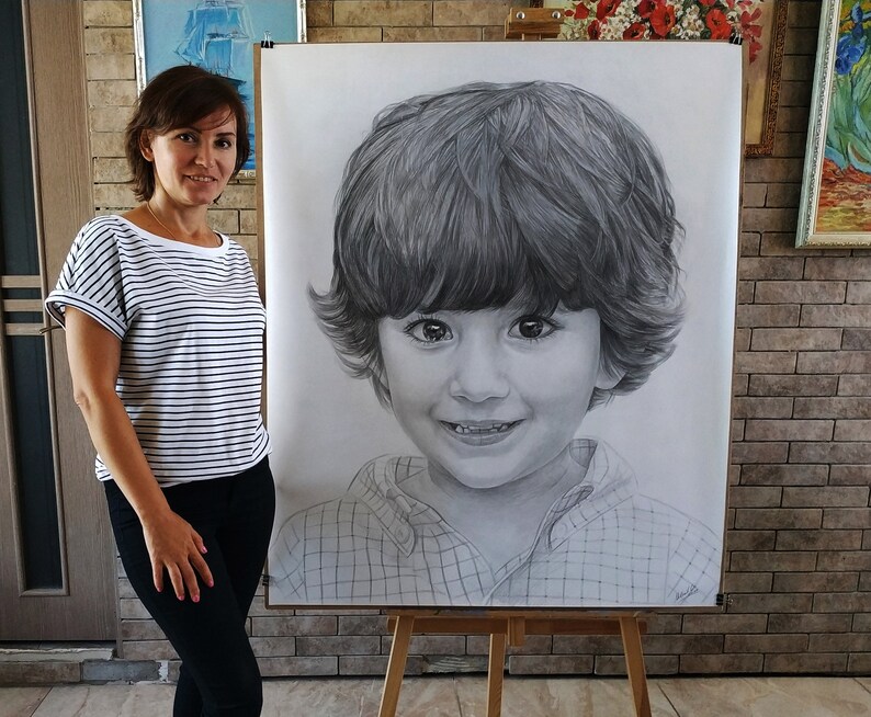 May include: A black and white pencil drawing of a young boy with short brown hair, wearing a plaid shirt. The drawing is on a large piece of paper and is being held up by a woman.