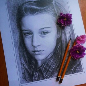 Puede incluir: Un dibujo a l&aacute;piz de una ni&ntilde;a joven con el pelo largo, que lleva una camisa a cuadros. El dibujo est&aacute; sobre un fondo blanco con dos flores moradas y dos l&aacute;pices.