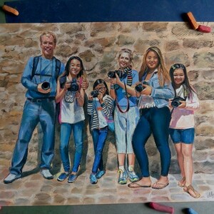 K&ouml;nnte beinhalten: Eine Pastellzeichnung einer siebenk&ouml;pfigen Familie, die vor einer Steinmauer posiert. Die Familie tr&auml;gt alle Freizeitkleidung und h&auml;lt Kameras in der Hand. Die Zeichnung ist in einem realistischen Stil gehalten und f&auml;ngt die W&auml;rme und Freude der Familie ein.