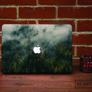 Könnte beinhalten: Ein Laptop mit einem Wald- und Nebeldesign. Der Laptop hat ein weißes Apple-Logo auf dem Deckel.