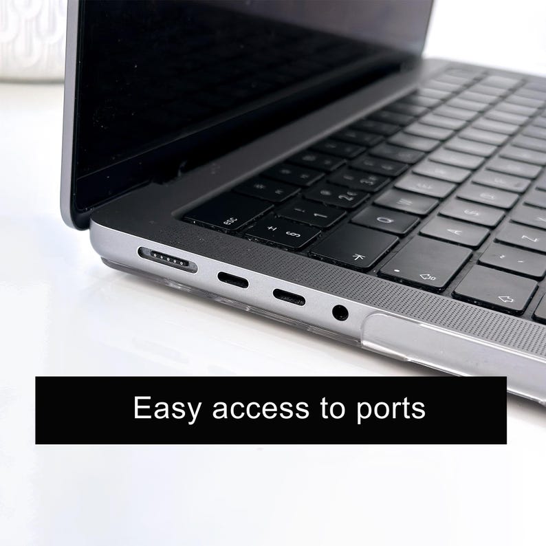 May include: A silver laptop with a black keyboard and a clear protective case installed. The side of the laptop features a magnetic charging port, two USB-C ports, and a headphone jack. The text "Easy access to ports" is displayed below.