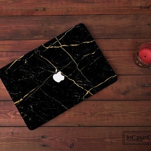 Peut inclure: Peau de protection d'ordinateur portable noire avec un motif de marbre doré. Le logo Apple est visible sur la peau.