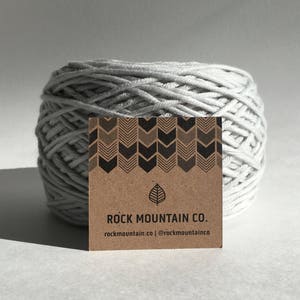Może przedstawiać: Brązowa karta z czarno-białym wzorem strzałek i tekstem "Rock Mountain Co." z adresem strony internetowej "rockmountain.co" i nazwą profilu w mediach społecznościowych "@rockmountainco".