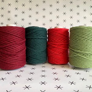 May include: Four spools of cotton rope in red, green, red, and green colors. The spools are arranged in a row on a white background with a black star pattern.