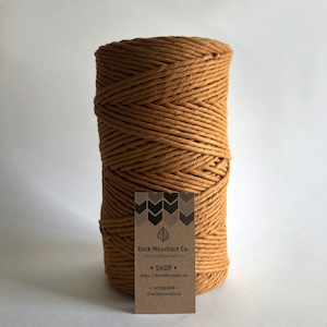 May include: A spool of thick, brown cotton rope. The rope is wound tightly and has a natural, rustic look. A business card for Rock Mountain Co. is in front of the spool. The card has a leaf design and the text "Rock Mountain Co. info@rockmountain.co SHOP https://rockmountain.co INSTAGRAM @rockmountainco"