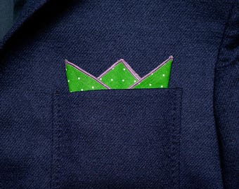 May include: A green pocket square with white polka dots folded into a crown shape in a navy blue suit jacket pocket.