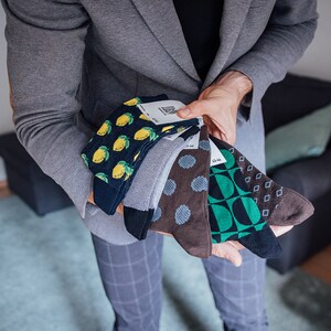 May include: A collection of five pairs of colorful socks with different patterns. The socks feature lemons, polka dots, geometric shapes, and a blue and green design.