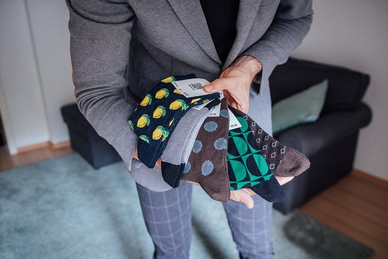 May include: A collection of five pairs of colorful socks with different patterns. The socks feature lemons, polka dots, geometric shapes, and a blue and green design.