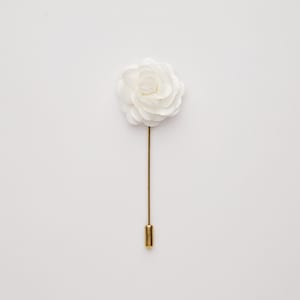 May include: A white fabric flower lapel pin with a gold stem and pin.