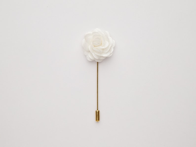 May include: A white fabric flower lapel pin with a gold stem and pin.