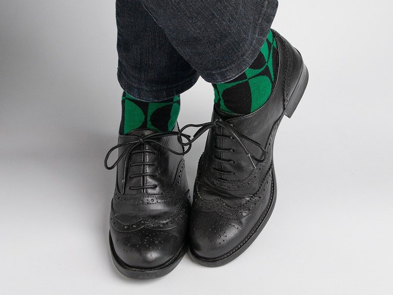 May include: Black leather oxford shoes with brogue detailing. The shoes are worn with green and black patterned socks.