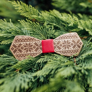 May include: A wooden bow tie with a red leather strap and a patterned design. The bow tie is on a green background.