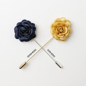 May include: Two fabric flower lapel pins with gold and silver needles. The flowers are navy blue and gold.