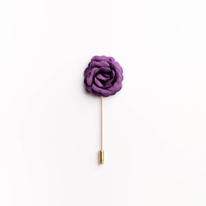 May include: A purple fabric rose boutonniere with a gold pin.