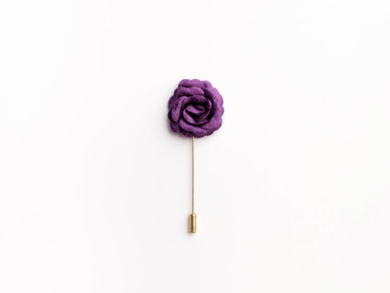 May include: A purple fabric rose boutonniere with a gold pin.