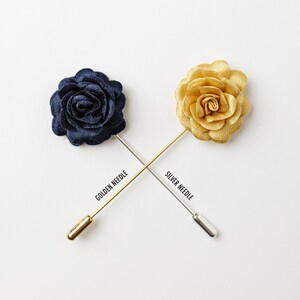 two decorative pins, one with a blue flower and the other with a gold flower, arranged diagonally across a white background.