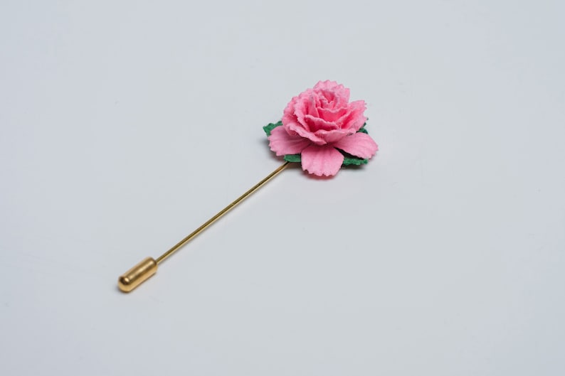 May include: A gold pin with a pink fabric rose on top. The rose has green leaves.