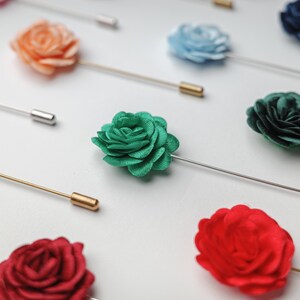 a close-up view of several colorful pin badges, including red, green, blue, and orange roses, arranged on a white background.