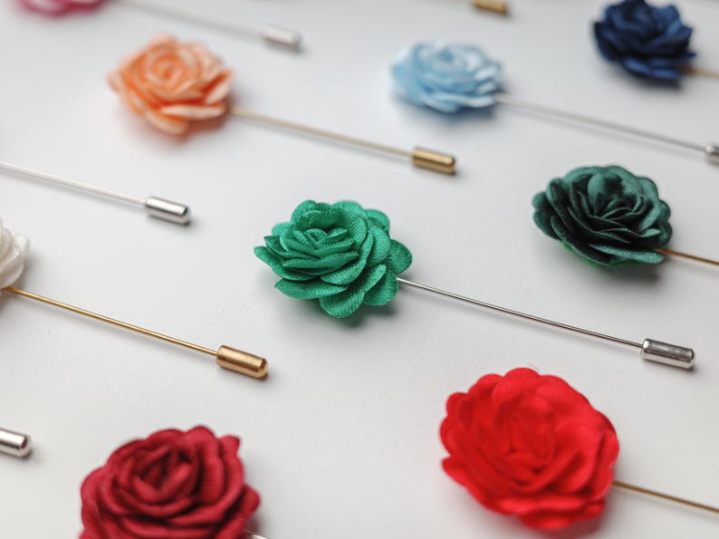 a close-up view of several colorful pin badges, including red, green, blue, and orange roses, arranged on a white background.
