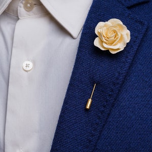 May include: A white rose boutonniere with a gold pin, worn on a blue blazer.