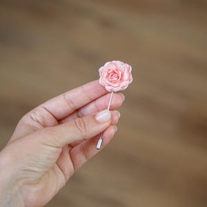 A hand holding a small pink flower pin against a blurred wooden background.