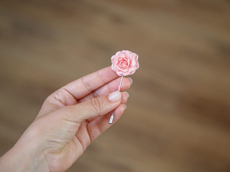 A hand holding a small pink flower pin against a blurred wooden background.