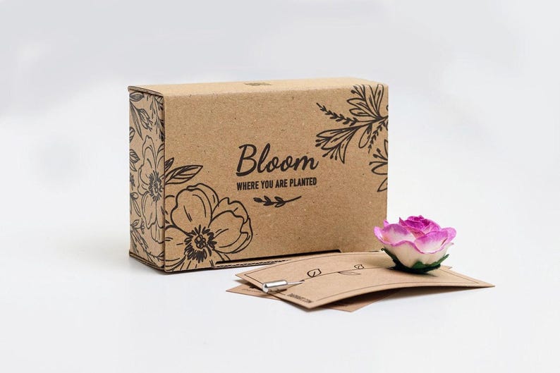 A cardboard box with a floral design and the text "Bloom" printed on it, along with a small pink rose-shaped object and some brown paper cards.