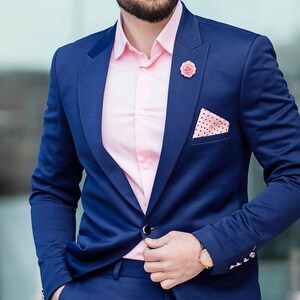 A man in a navy blue suit with a gold lapel pin stands in front of a glass building.