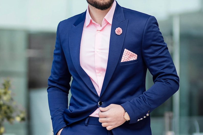 A man in a navy blue suit with a gold lapel pin stands in front of a glass building.