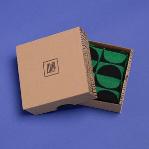 May include: A brown cardboard box with a black and green patterned fabric inside. The box has the word "DAIT" printed on it in black.