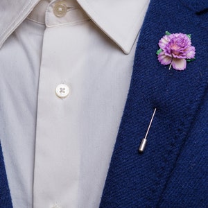 May include: A blue blazer with a white button-down shirt and a purple flower lapel pin.