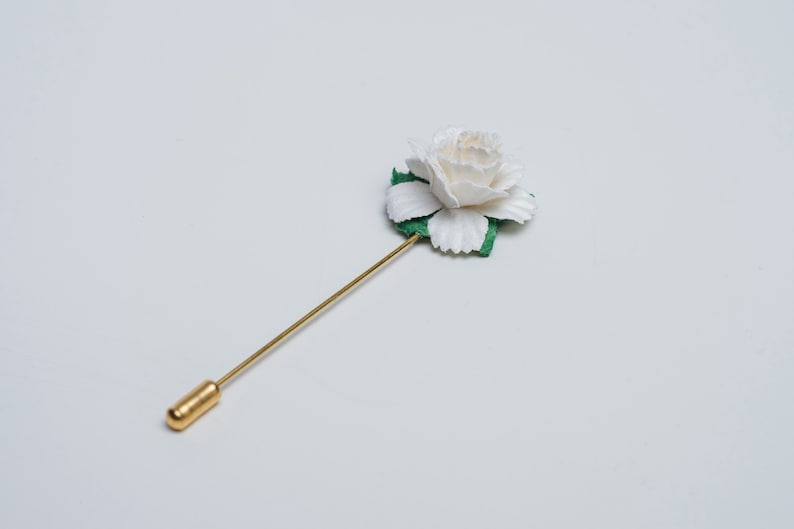 May include: A white flower with green leaves on a gold pin.