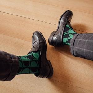 May include: A pair of black leather loafers with green and black patterned socks. The socks have a geometric design.
