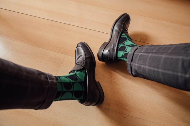 May include: A pair of black leather loafers with green and black patterned socks. The socks have a geometric design.