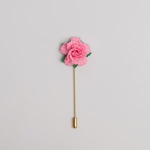May include: A pink flower lapel pin with green leaves and a gold stem.