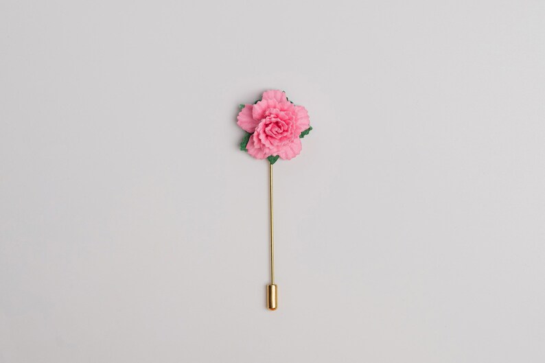 May include: A pink flower lapel pin with green leaves and a gold stem.